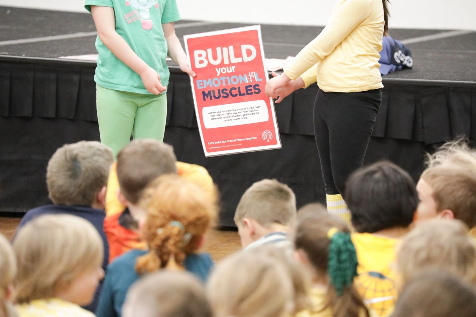 Children holding a red Build your emotional muscles sign at a Gotcha4Life school session